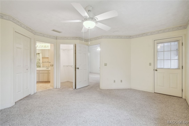 unfurnished bedroom with ceiling fan, light colored carpet, a spacious closet, and ensuite bath