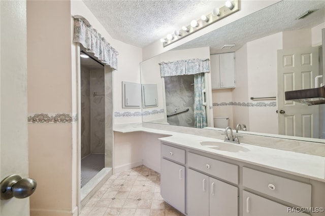 bathroom featuring a textured ceiling, vanity, toilet, and tiled shower