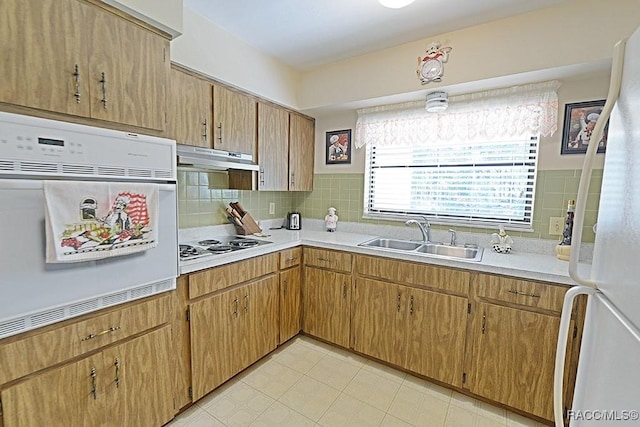 kitchen with under cabinet range hood, white appliances, a sink, light countertops, and backsplash