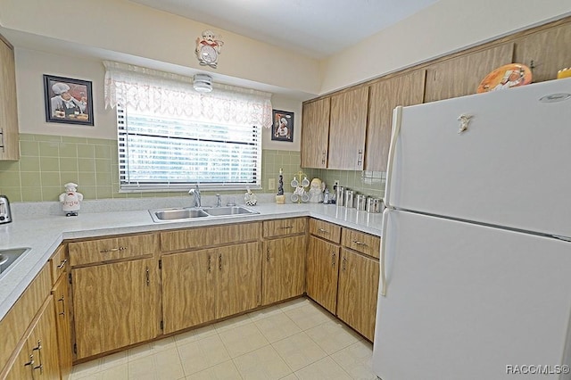 kitchen featuring a sink, light countertops, freestanding refrigerator, tasteful backsplash, and brown cabinetry