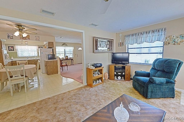 carpeted living room with ceiling fan, tile patterned flooring, and visible vents