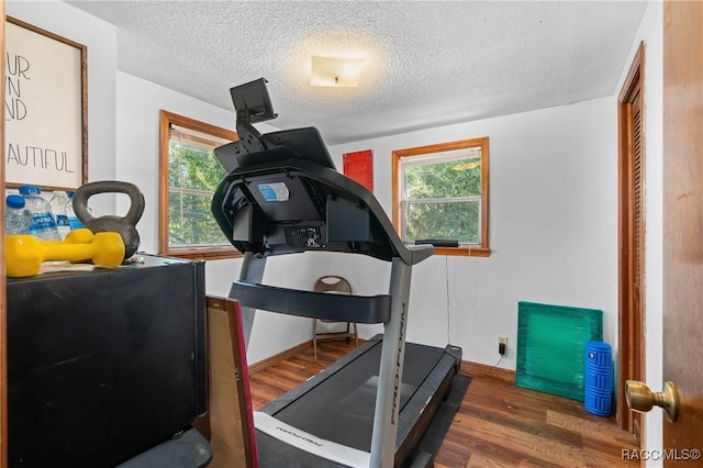 workout area with dark wood-type flooring, a wealth of natural light, and a textured ceiling