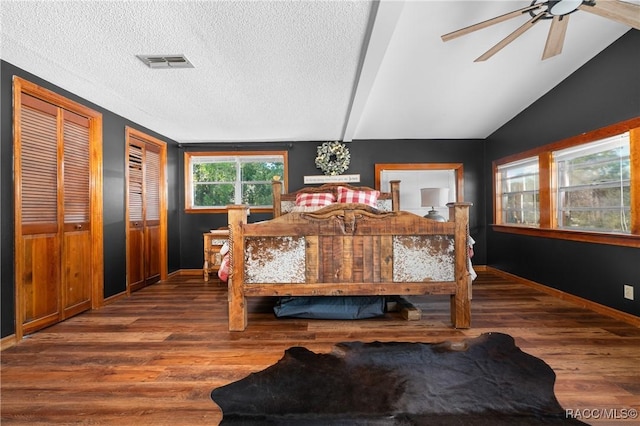 bedroom with two closets, wood-type flooring, a textured ceiling, and vaulted ceiling