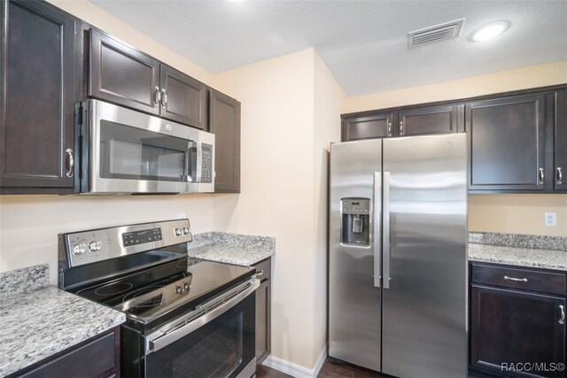 kitchen featuring light stone countertops, appliances with stainless steel finishes, and dark brown cabinets