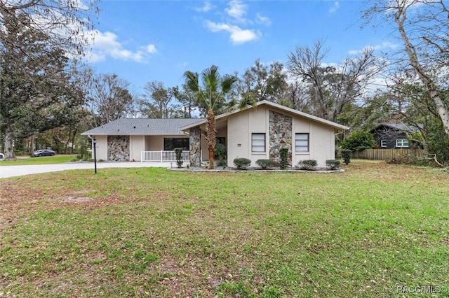 mid century modern with fence, covered porch, stone siding, and a front yard