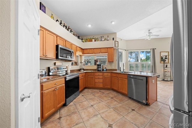 kitchen with kitchen peninsula, stainless steel appliances, ceiling fan, sink, and light tile patterned flooring