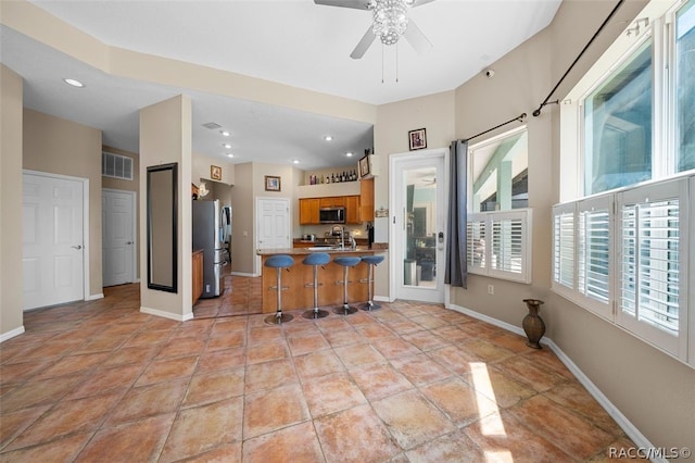 kitchen with ceiling fan, sink, stainless steel appliances, kitchen peninsula, and a kitchen bar