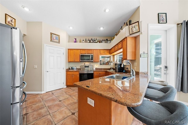 kitchen with stone counters, sink, stainless steel appliances, kitchen peninsula, and a kitchen bar