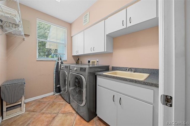 clothes washing area with washing machine and dryer, sink, light tile patterned flooring, and cabinets