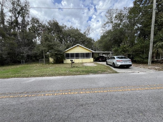 view of front of house featuring concrete driveway, a carport, a front yard, and a sunroom