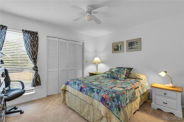 bedroom featuring ceiling fan, a closet, light colored carpet, and a textured ceiling