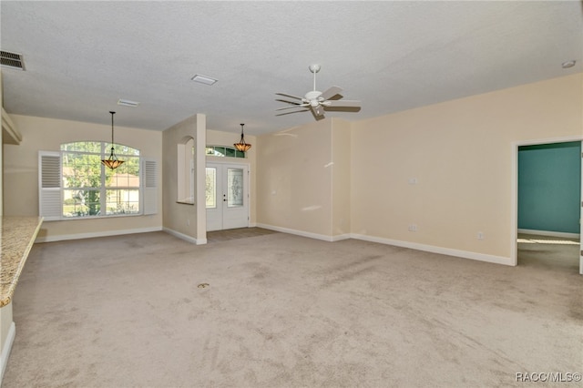 carpeted empty room featuring french doors, ceiling fan with notable chandelier, and a textured ceiling