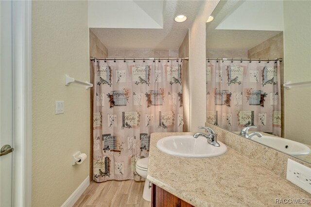 bathroom with walk in shower, vanity, a textured ceiling, hardwood / wood-style floors, and toilet