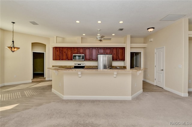 kitchen with pendant lighting, ceiling fan, a kitchen island, light colored carpet, and stainless steel appliances