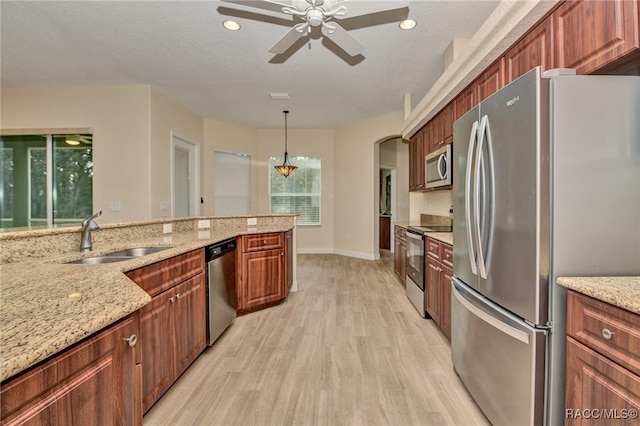 kitchen with sink, hanging light fixtures, stainless steel appliances, light stone counters, and light wood-type flooring