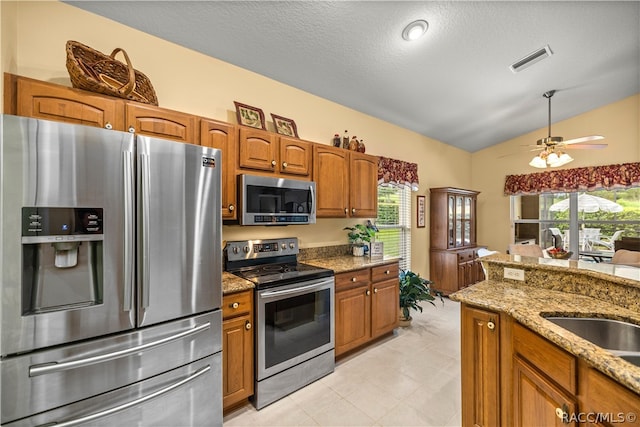 kitchen with ceiling fan, light stone counters, a textured ceiling, lofted ceiling, and appliances with stainless steel finishes