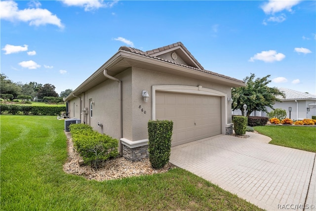 view of side of property with a lawn, a garage, and central AC