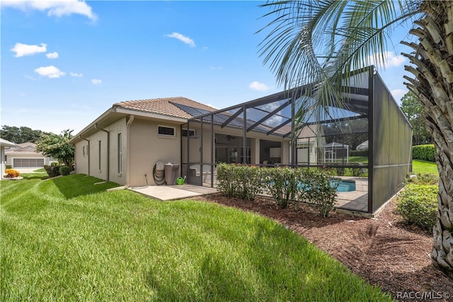 rear view of property featuring a lawn, glass enclosure, and a patio