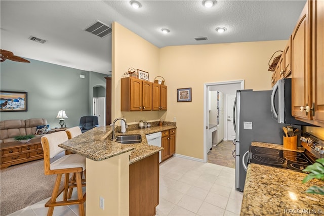 kitchen featuring sink, stainless steel appliances, light stone counters, vaulted ceiling, and a breakfast bar area