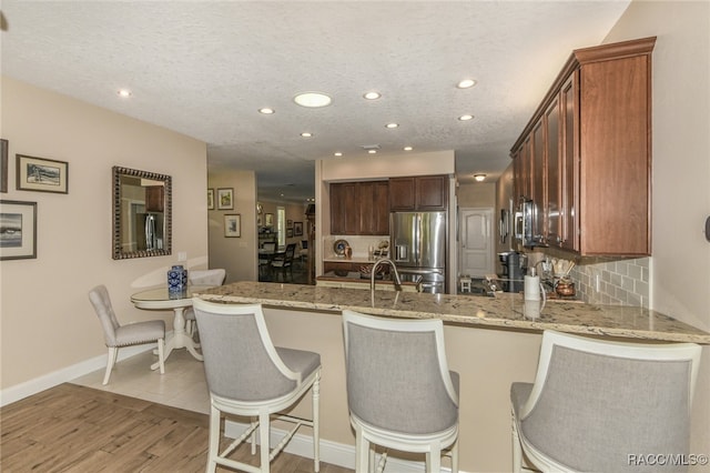 kitchen featuring kitchen peninsula, stainless steel appliances, a textured ceiling, and light wood-type flooring