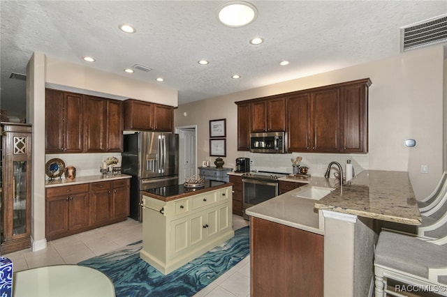 kitchen with sink, kitchen peninsula, a textured ceiling, a breakfast bar area, and appliances with stainless steel finishes