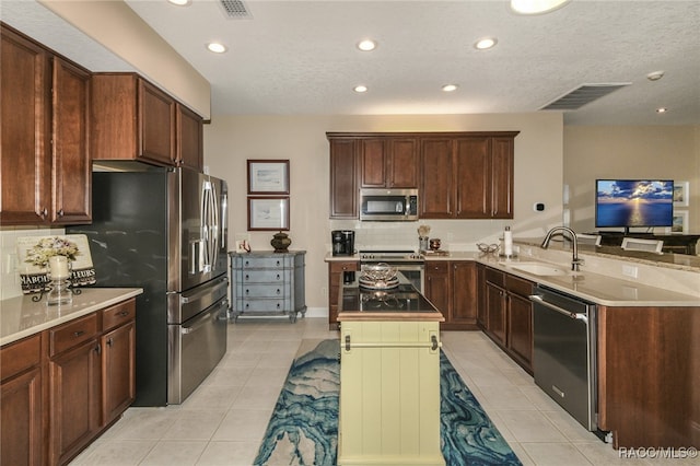 kitchen with kitchen peninsula, light tile patterned floors, sink, and appliances with stainless steel finishes