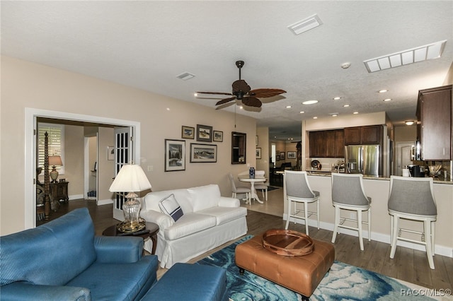 living room with dark hardwood / wood-style floors, ceiling fan, and a textured ceiling