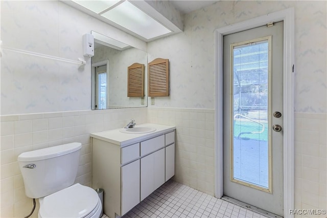 bathroom with vanity, toilet, tile walls, and a wealth of natural light