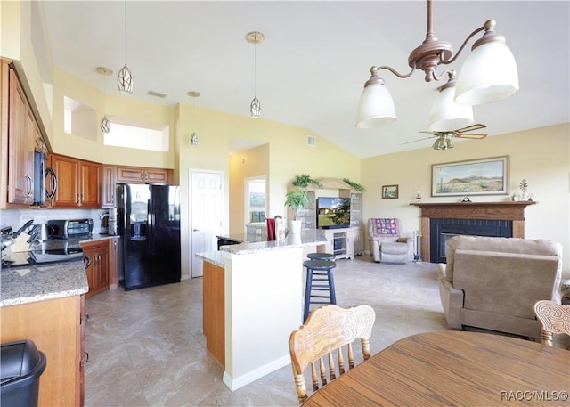 kitchen with pendant lighting, ceiling fan with notable chandelier, light stone countertops, a fireplace, and black fridge with ice dispenser