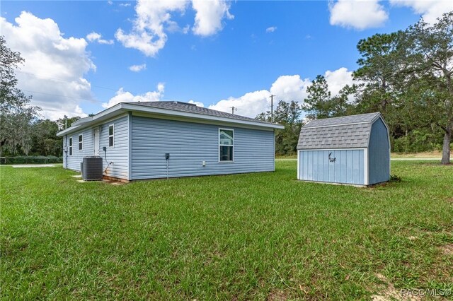 rear view of house featuring a lawn, a storage unit, and central AC