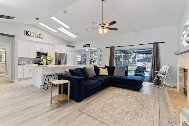 living room with ceiling fan, light hardwood / wood-style floors, a fireplace, and vaulted ceiling