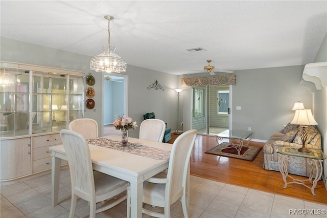 dining area featuring ceiling fan with notable chandelier, a textured ceiling, and light wood-type flooring