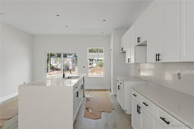 kitchen with an island with sink, sink, white cabinetry, and light hardwood / wood-style floors