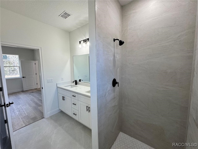 bathroom featuring a textured ceiling, vanity, and tiled shower