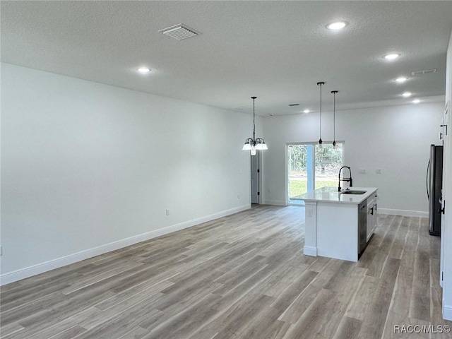 kitchen featuring a center island with sink, sink, a textured ceiling, appliances with stainless steel finishes, and decorative light fixtures