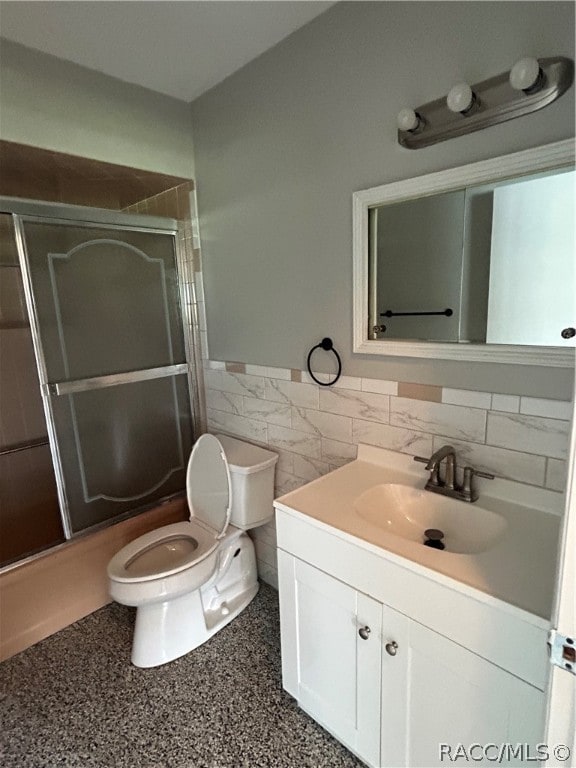 full bathroom featuring vanity, toilet, shower / bath combination with glass door, and tile walls