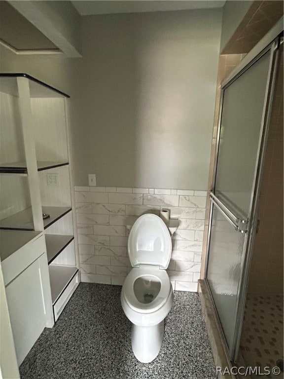 bathroom with a shower with door, tile walls, and toilet