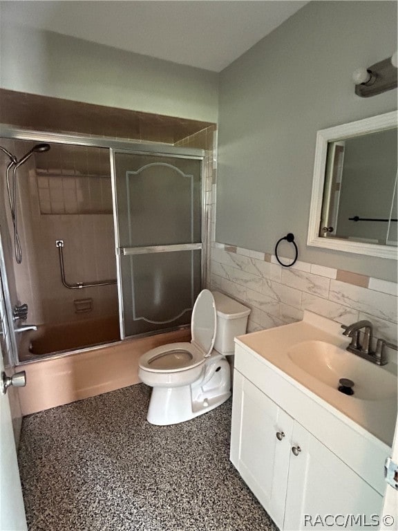 full bathroom featuring vanity, bath / shower combo with glass door, tile walls, and toilet