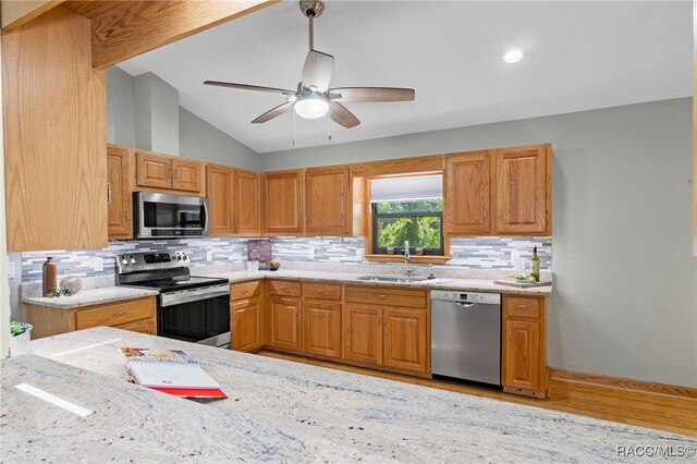 kitchen with vaulted ceiling, appliances with stainless steel finishes, light stone countertops, and sink