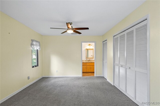 unfurnished bedroom featuring ensuite bathroom, carpet flooring, two closets, and ceiling fan