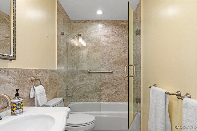 full bathroom with tile walls, sink, toilet, and combined bath / shower with glass door