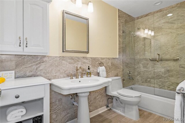 bathroom featuring hardwood / wood-style floors, tile walls, shower / bath combination with glass door, and toilet