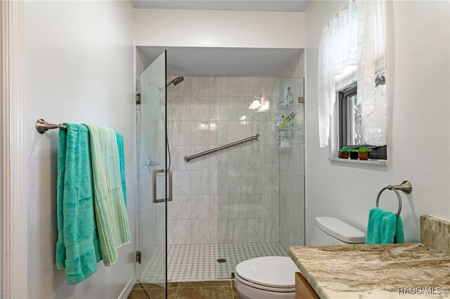 bathroom featuring tile patterned flooring, vanity, a shower with shower door, and toilet