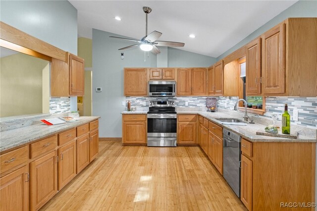 kitchen featuring light stone counters, sink, vaulted ceiling, and appliances with stainless steel finishes