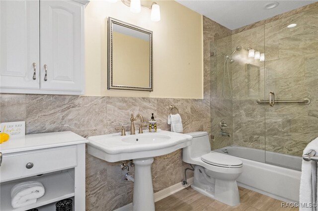 bathroom featuring tile walls, hardwood / wood-style flooring, enclosed tub / shower combo, and toilet