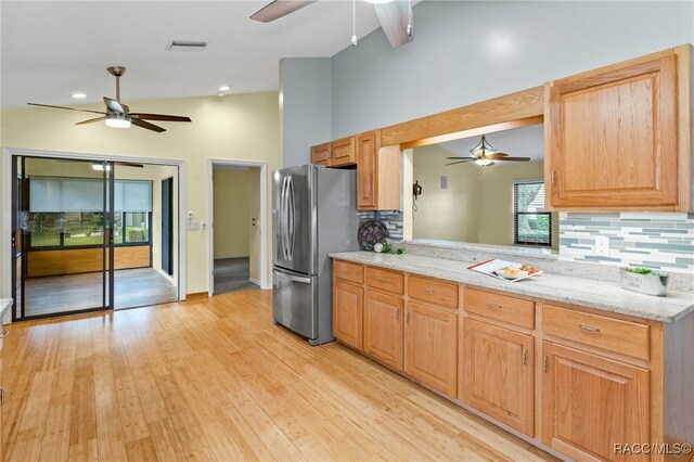 kitchen with stainless steel fridge, ceiling fan, light stone countertops, light hardwood / wood-style floors, and decorative backsplash