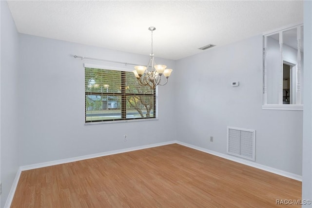 empty room featuring wood-type flooring, a textured ceiling, and a chandelier