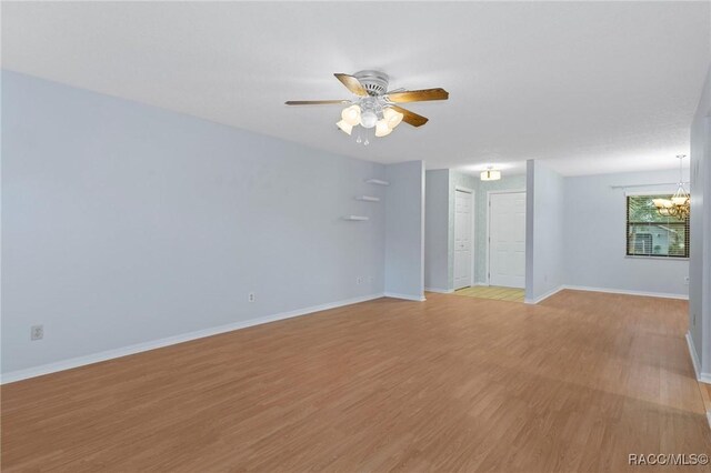 spare room featuring ceiling fan with notable chandelier and light hardwood / wood-style flooring