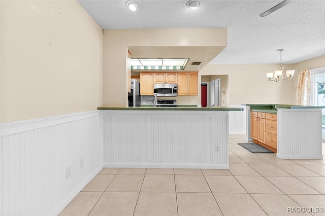 kitchen featuring kitchen peninsula, hanging light fixtures, appliances with stainless steel finishes, and an inviting chandelier