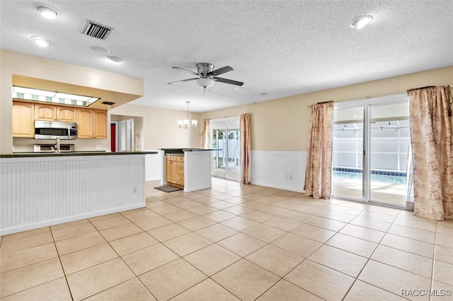 kitchen with light brown cabinets, hanging light fixtures, a textured ceiling, light tile patterned flooring, and ceiling fan with notable chandelier